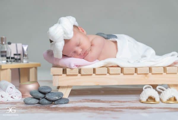 Newborn wearing white robe sleeping on wood bed.